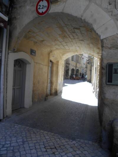 Rue étroite pavée passant sous une large voûte en pierre médiévale comprenant à gauche deux portes d'entrée